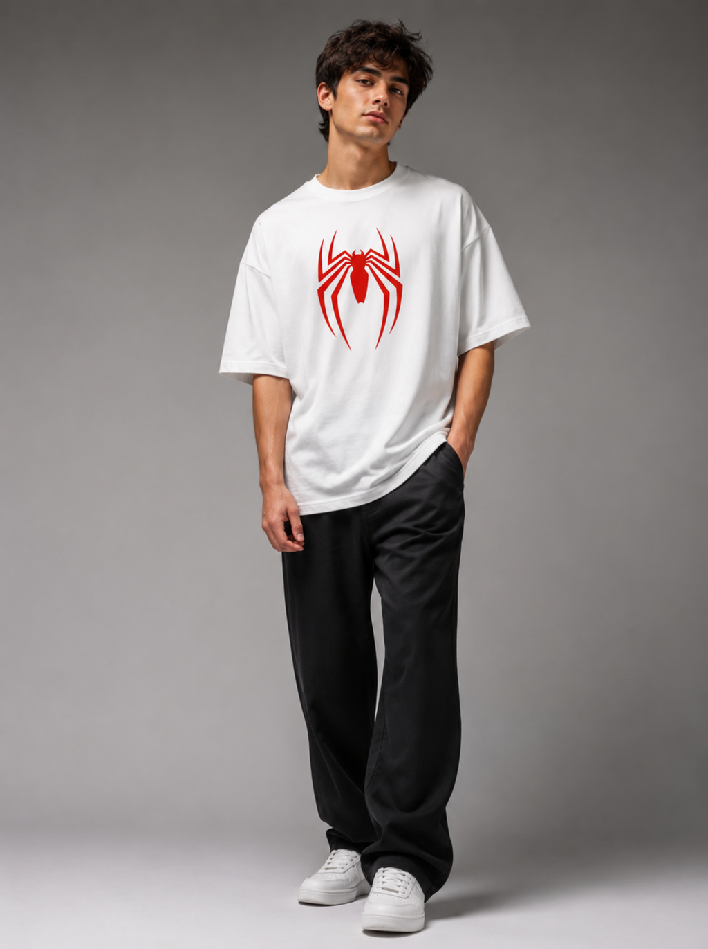 A man modeling an oversized white t-shirt with a red spider logo on the chest, paired with black sweatpants and white sneakers, against a gray studio background.